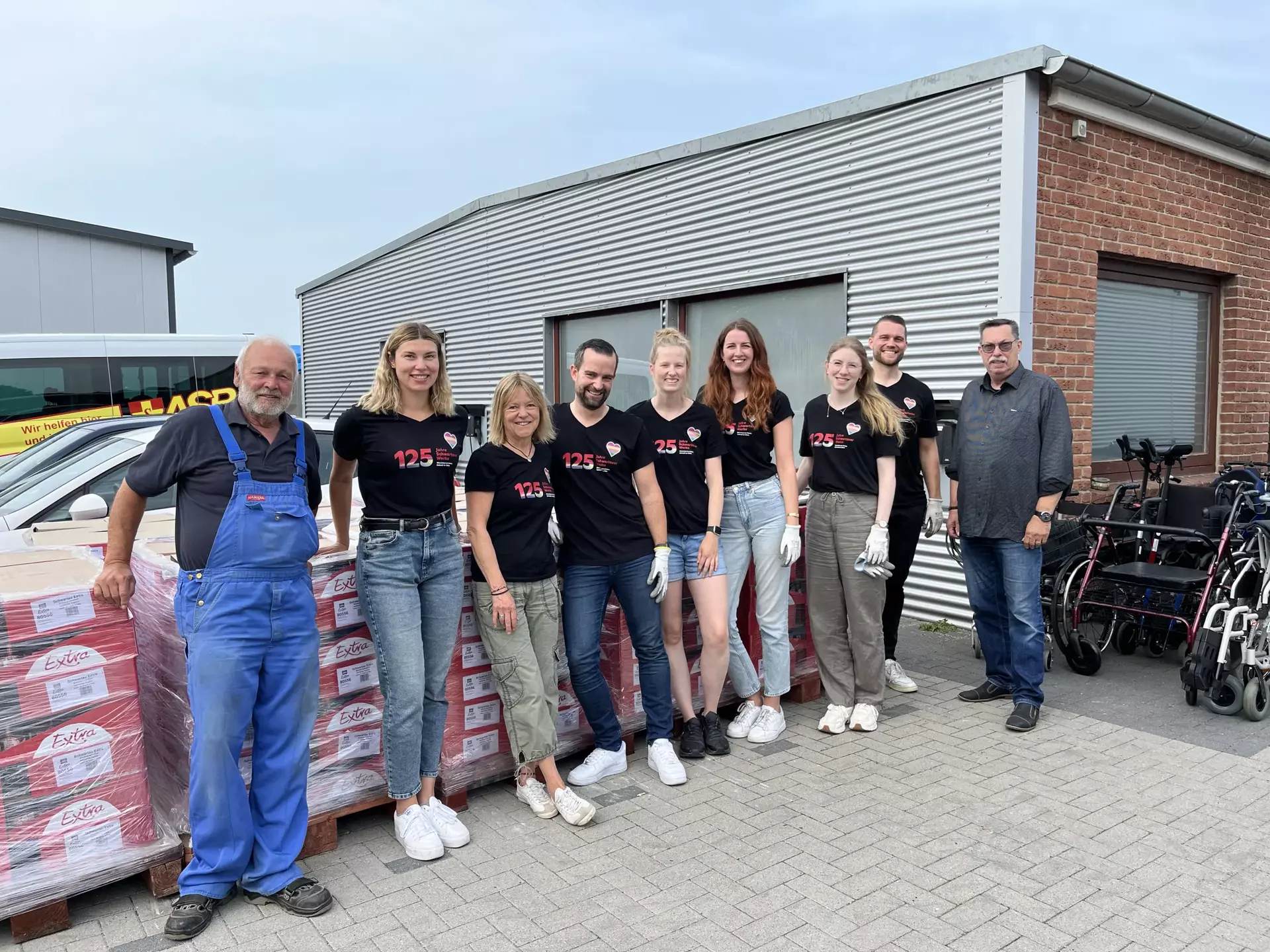 Zu sehen sind sieben Schwartau Kolleg*innen und zwei Mitarbeiter*innen vom ASB, die in einer Gruppe draußen vor Paletten mit Schwartau-Produkten stehen.