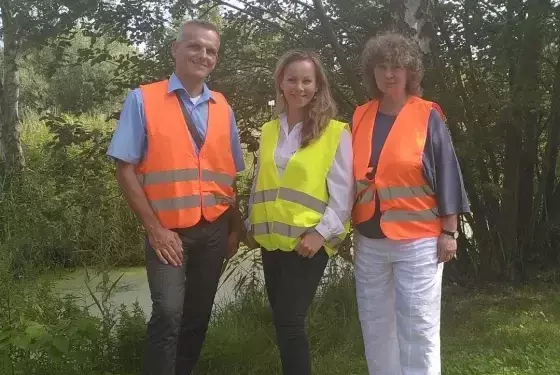 Das Bild zeigt drei Personen mit Warnwesten, die auf einer Wiese vor Bäumen stehen. In der Mitte steht unsere Nachhaltigkeitsmanagerin Julia Schäfer.