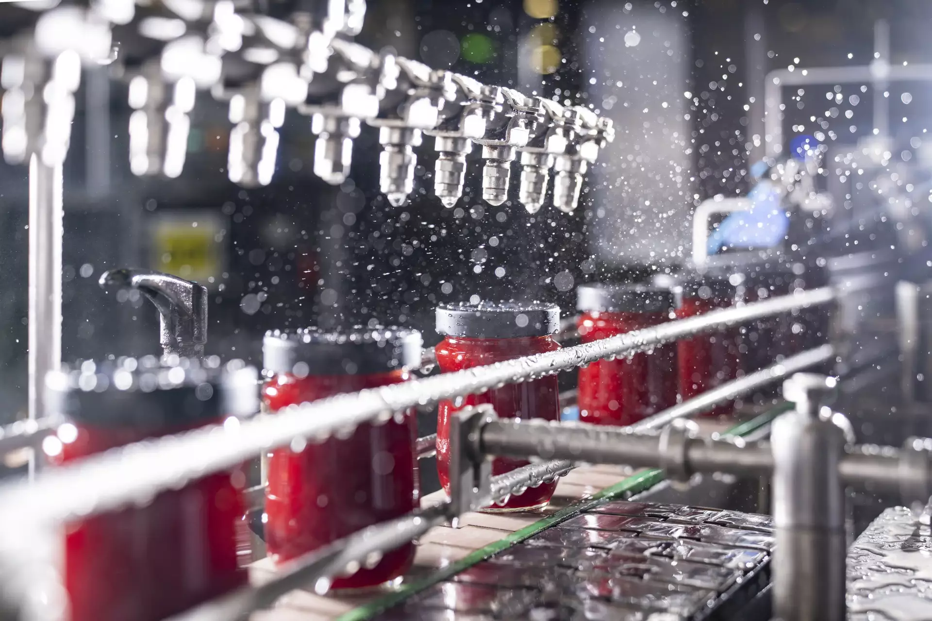 Frisch befüllte Gläser mit Erdbeerkonfitüre auf einem Förderband, noch ohne Etikett