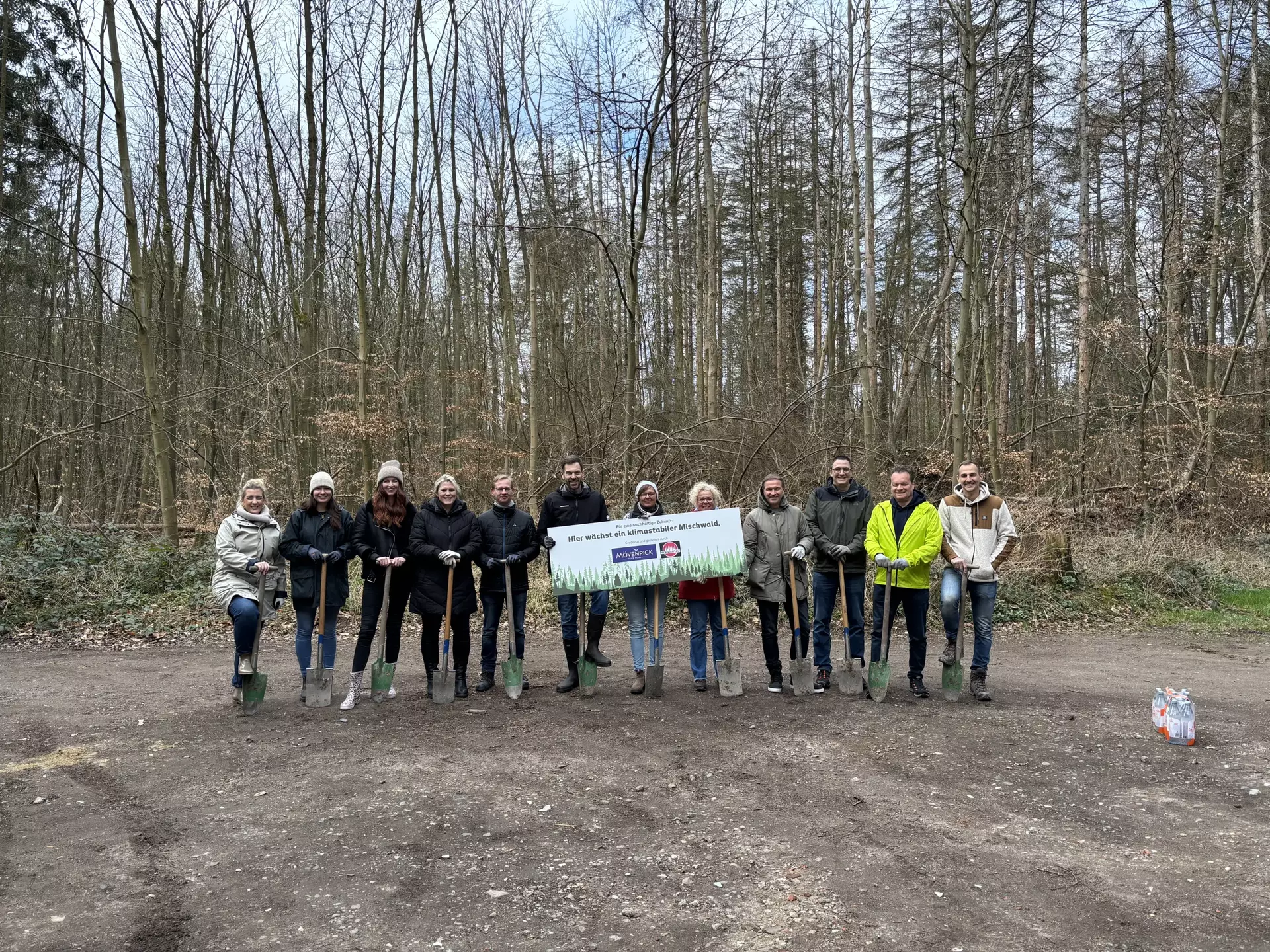 Ein Gruppenfoto der Kolleg*innen, die an der Pflanzaktion teilgenommen haben. Zwei in der Mitte halten einen Banner mit der Aufschrift: "Für eine nachhaltige Zukunft: Hier wächst ein klimastabiler Mischwald".