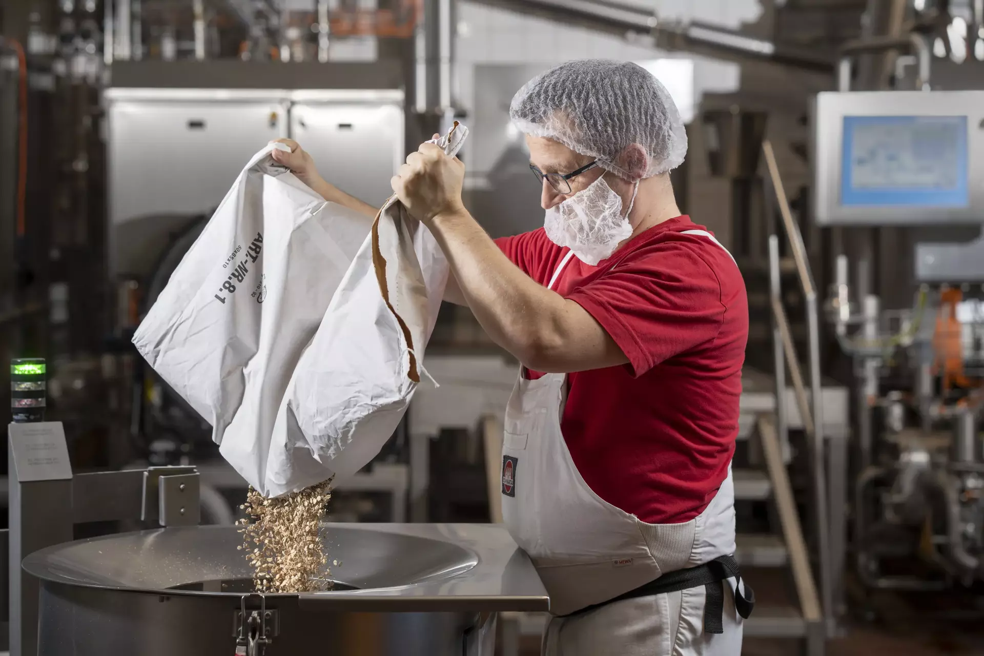 Ein Mitarbeiter in Arbeitskleidung befüllt einen Kessel mit Haferflocken aus einem Papiersack