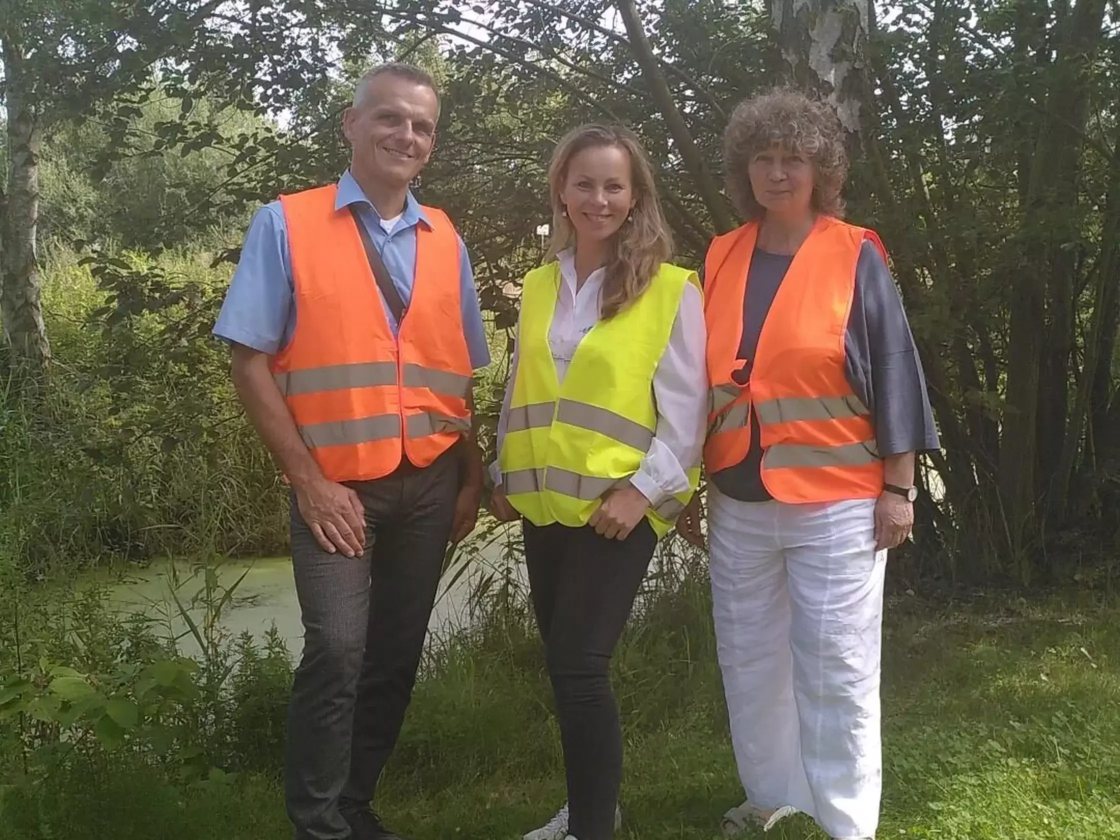 Das Bild zeigt drei Personen mit Warnwesten, die auf einer Wiese vor Bäumen stehen. In der Mitte steht unsere Nachhaltigkeitsmanagerin Julia Schäfer.