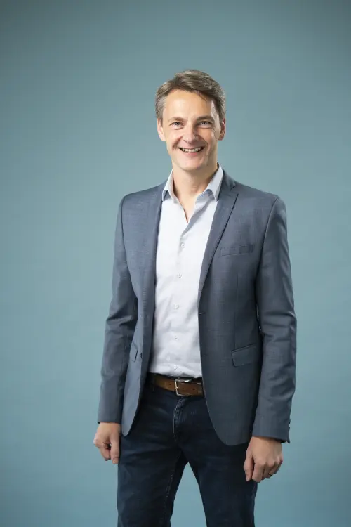 Mann in Jeans und blauem Sacko vor einer Leinwand, freundliches Lächeln