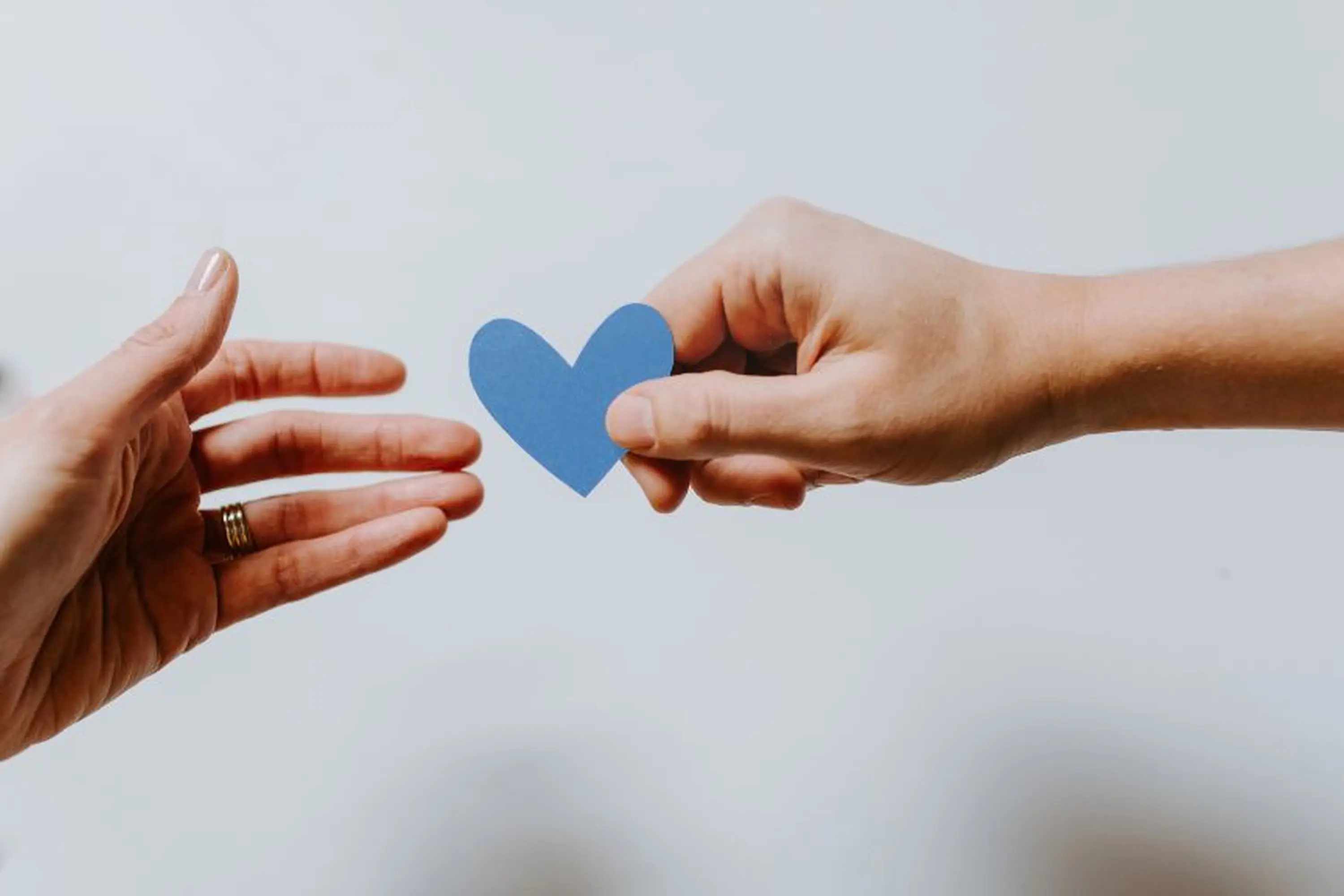 Zwei Hände tauschen ein gebasteltes Herz aus.