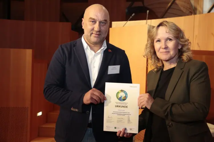 Das Bild zeigt zwei Personen, die schick angezogen sind und eine Urkunde überreichen. Auf der linken Seite steht unser Kollege Kai Maack, welcher von der Umweltministerin Steffi Lemke die Urkunde für "Die Lieferkette lebt" überreicht bekommt.